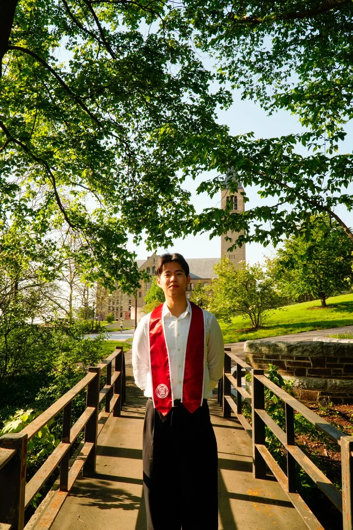 Matthew at his Cornell graduation, in a red stole on a wooden bridge